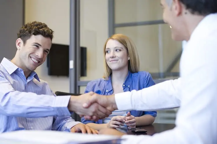 A smiling couple shaking hands with a loan officer