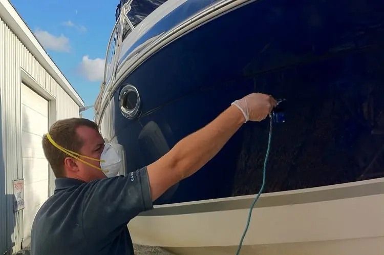 A man in a mask and gloves sanding the hull of a large boat