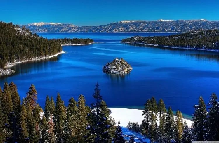 Blue lake surrounded by pine forest and snowy mountains